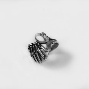 May include: A silver ring with a wing design and a circular cutout in the center.