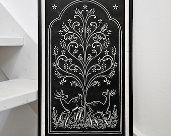 May include: Black and white framed art print featuring a stylized tree with floral details and two deer. The artwork has a symmetrical design with a dark background and white linework. The frame is black.