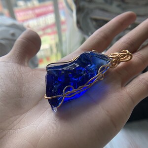 May include: A blue glass pendant wrapped in gold wire. The pendant is shaped like a rough, irregular piece of glass.