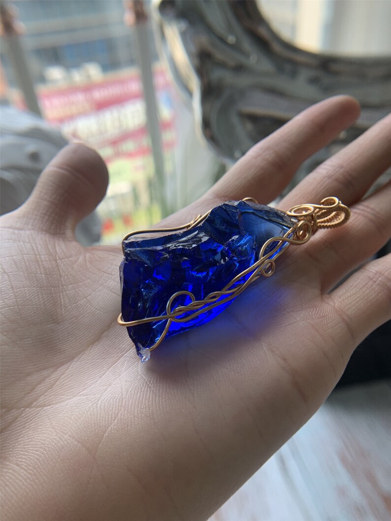 May include: A blue glass pendant wrapped in gold wire. The pendant is shaped like a rough, irregular piece of glass.