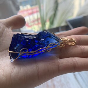 May include: A deep blue glass pendant wrapped in gold wire, creating a unique and intricate design.