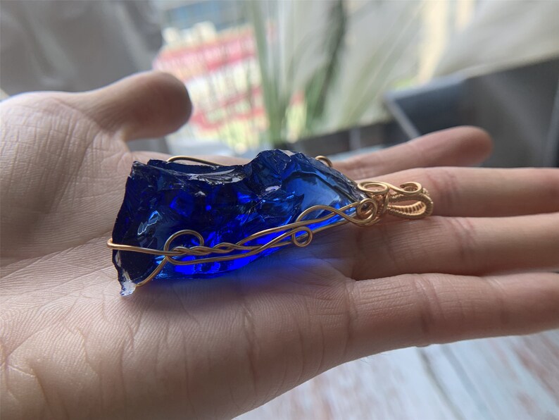 May include: A deep blue glass pendant wrapped in gold wire, creating a unique and intricate design.