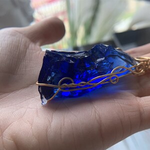 May include: A deep blue glass pendant wrapped in gold wire. The pendant has a rough, irregular shape, reminiscent of a gemstone.