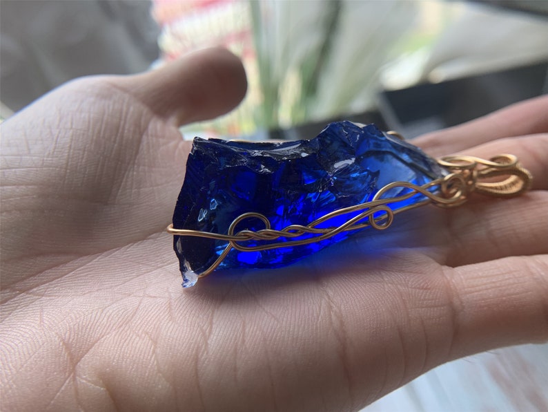 May include: A deep blue glass pendant wrapped in gold wire. The pendant has a rough, irregular shape, reminiscent of a gemstone.
