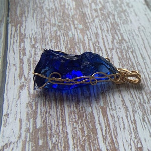 May include: A deep blue glass pendant wrapped in gold wire with a decorative bail.