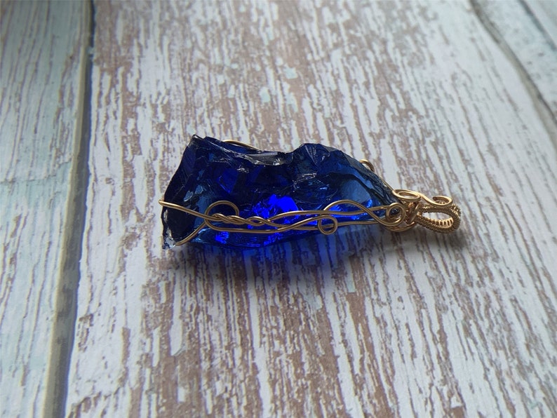 May include: A deep blue glass pendant wrapped in gold wire with a decorative bail.