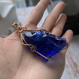May include: A deep blue glass pendant wrapped in gold wire. The pendant is shaped like a rough, irregular crystal.