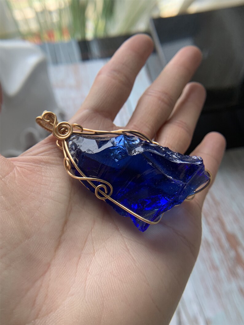 May include: A deep blue glass pendant wrapped in gold wire. The pendant is shaped like a rough, irregular crystal.