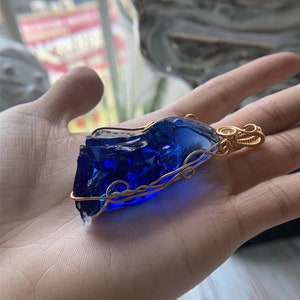 May include: A deep blue glass pendant wrapped in gold wire. The pendant has a rough, irregular shape, reminiscent of a gemstone.
