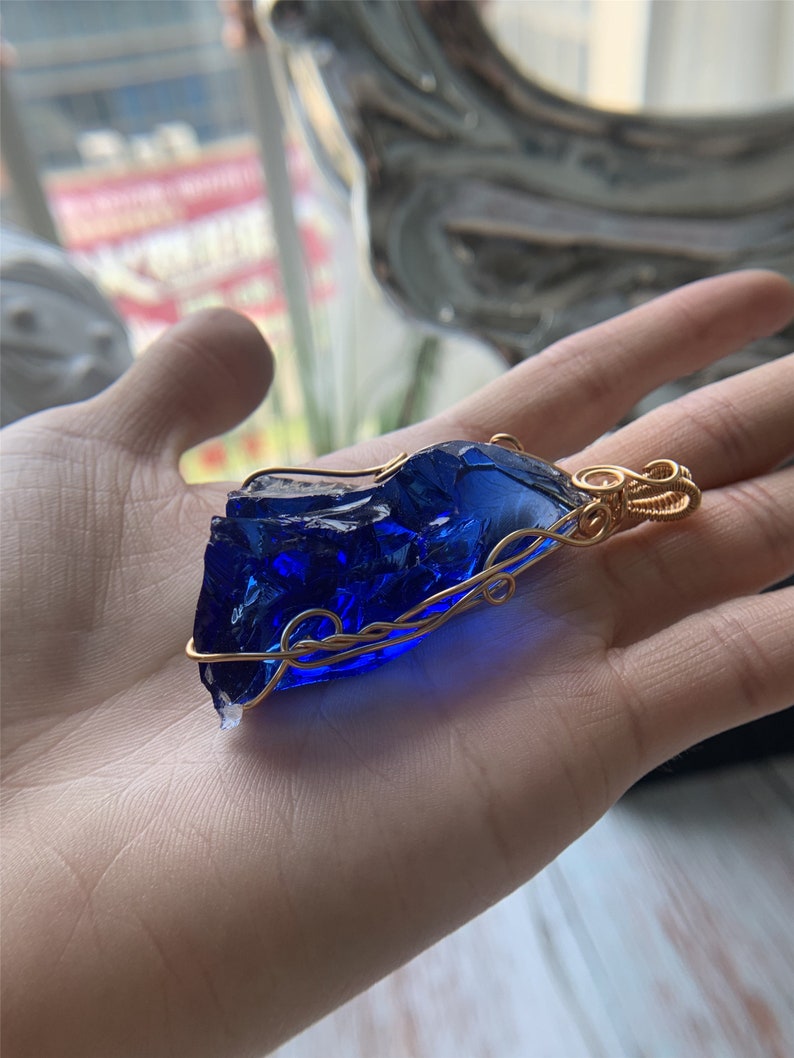 May include: A deep blue glass pendant wrapped in gold wire. The pendant has a rough, irregular shape, reminiscent of a gemstone.