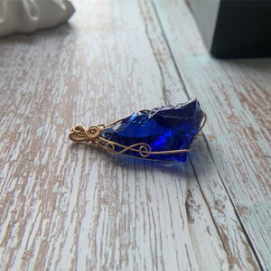 May include: A deep blue glass pendant wrapped in gold wire. The pendant is shaped like a rough, irregular stone.