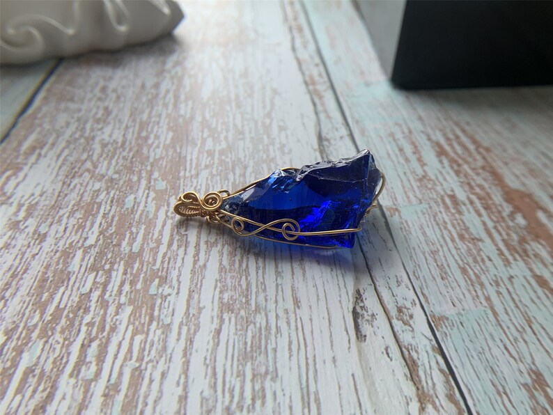 May include: A deep blue glass pendant wrapped in gold wire. The pendant is shaped like a rough, irregular stone.