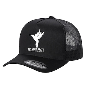 May include: A black trucker hat with a mesh back and a flat brim. The front panel features a white graphic of a hummingbird above the text SPENCER PRATT FOR MAYOR OF LOS ANGELES. A circular sticker on the brim reads SNAPBACK and other text.
