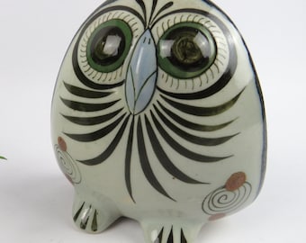 May include: A ceramic owl figurine with a rounded body and a whimsical design. The owl features large, expressive green eyes, a light blue beak, and black and white feather details. Decorative swirls and dots add to the charm of this handcrafted art piece.