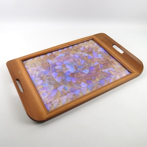 Puede incluir: Una bandeja rectangular de madera con un diseño decorativo de mariposas. La bandeja tiene un marco marrón claro con asas recortadas. El interior presenta un mosaico de alas de mariposa en tonos morados, azules y marrones.