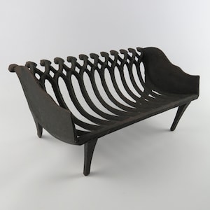 Peut inclure: Une grille de cheminée en fonte gris foncé présentant un design incurvé à lattes avec des sommets décoratifs en forme de volutes sur chaque barre verticale. La grille est soutenue par quatre pieds inclinés robustes et des panneaux latéraux pleins.