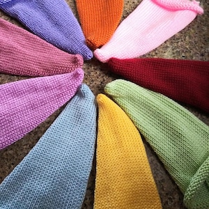 May include: A collection of ten knitted hats in various colors, including purple, pink, red, green, blue, yellow, and orange. The hats are arranged in a circle, with the tips of the hats pointing towards the center.