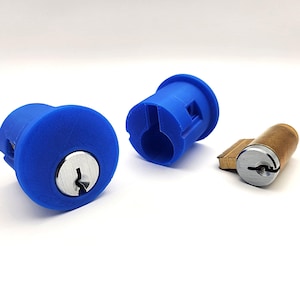 May include: Three blue cylindrical lock components and a brown and silver lock cylinder are displayed against a white background. The blue components have a keyhole and a circular design. The brown cylinder has a silver face.