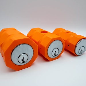 May include: Three bright orange, cylindrical objects with a hexagonal design. Each has a silver-colored, circular face with a keyhole. The objects are arranged in a row against a white background.