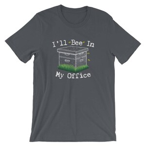 May include: Dark gray t-shirt with a white beehive and the text "I'll Bee In My Office" printed on the front.
