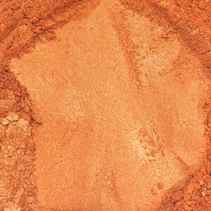 May include: A close-up of a pile of loose, shimmery copper mica powder. The powder has a fine texture and a warm, metallic sheen.