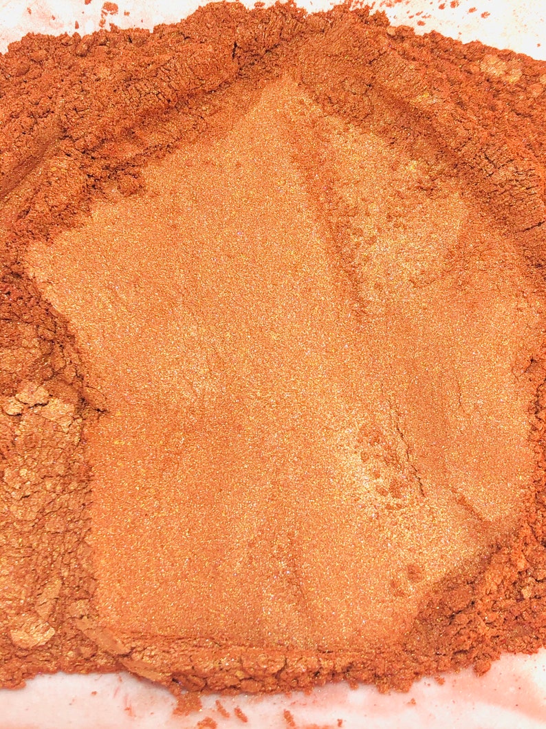 May include: A close-up of a pile of loose, shimmery copper mica powder. The powder has a fine texture and a warm, metallic sheen.