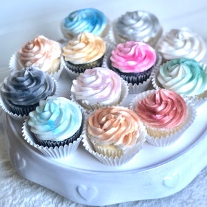 May include: A white cake stand with 12 cupcakes decorated with different colored frosting. The frosting is swirled and has a watercolor effect. The colors include blue, pink, gray, gold, and silver.