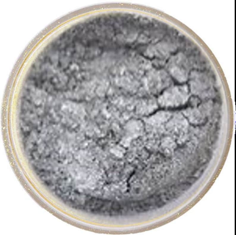 May include: A small round container of silver glitter makeup. The glitter is loose and has a slightly textured appearance.