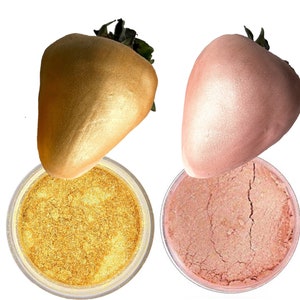 K&ouml;nnte beinhalten: Zwei Gl&auml;ser mit Kosmetik-Glitter, eines golden und eines rosa, mit einer goldenen und einer rosafarbenen Erdbeere auf jedem Glas.