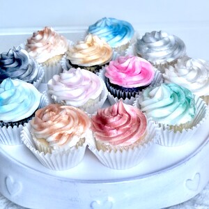 May include: A white cake stand with a variety of cupcakes decorated with different colored frosting. The cupcakes are decorated with shades of blue, pink, gray, and brown.