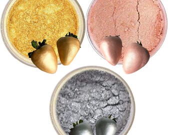 May include: Three containers of edible glitter in gold, rose gold, and silver. Each container has two decorative strawberry-shaped candies. The glitter has a fine, shimmering texture, perfect for decorating desserts and treats.