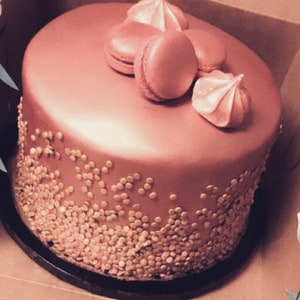 K&ouml;nnte beinhalten: Ein ros&eacute;goldener Kuchen, der mit goldenen Streuseln verziert ist und mit Macarons und Baiser-K&uuml;chlein belegt ist.