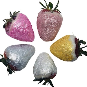 May include: Five strawberries dipped in white chocolate and covered in glitter. The strawberries are arranged in a circle. The glitter is pink, gold, and silver.