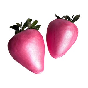 May include: Two pink, shiny, faux strawberries with green leaves.
