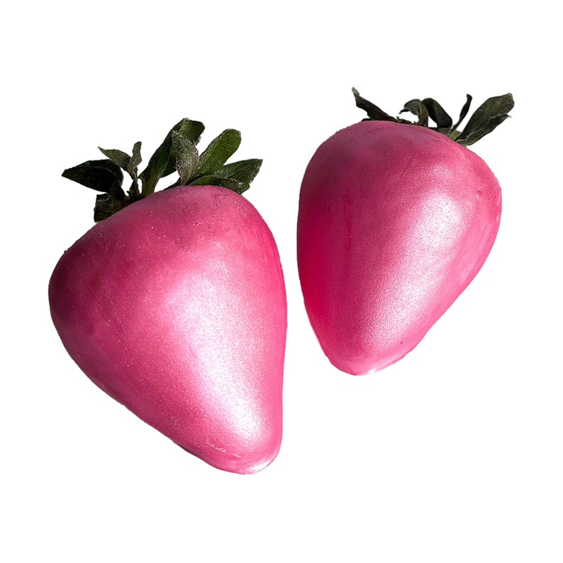 May include: Two pink, shiny, faux strawberries with green leaves.