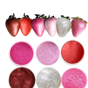 May include: Six small bowls of edible luster dust in various shades of pink, red, and silver. The dust is used for decorating cakes, cookies, and other desserts.