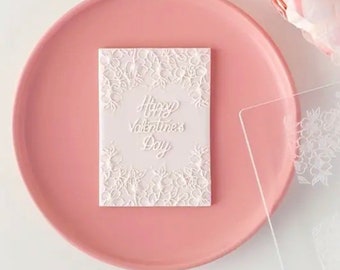 May include: A white card with a floral design and the text "Happy Valentine's Day" in a cursive font. The card is on a pink plate.