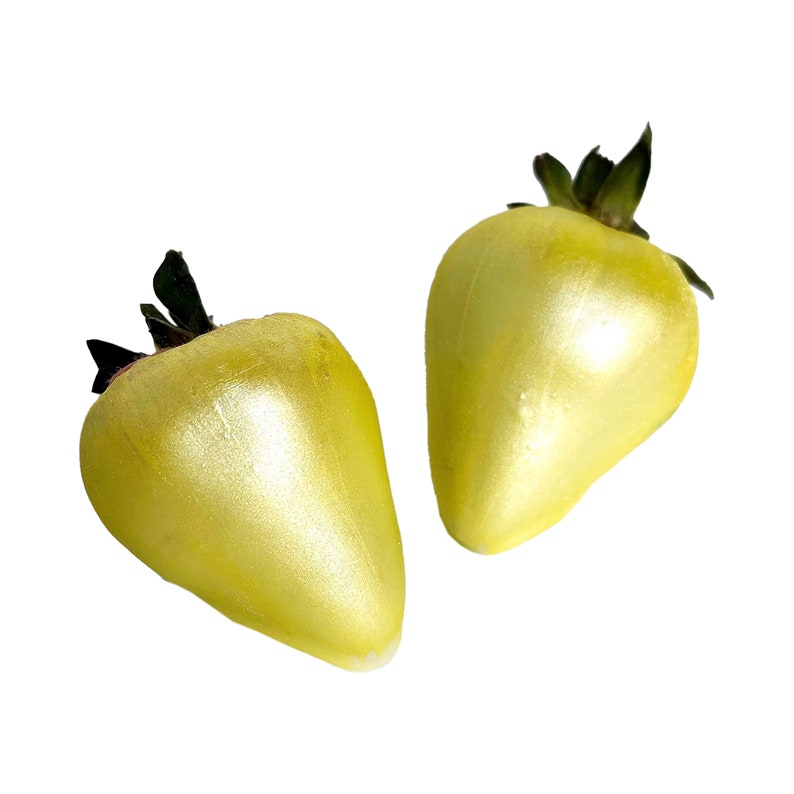 May include: Two yellow, shiny, strawberry-shaped candies with green stems.