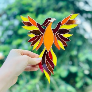 May include: A stained glass phoenix with red, orange, and yellow wings and tail. The phoenix is made of glass and has a copper frame.