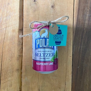 May include: A pink and white can of Polar Seltzer Raspberry Lime, calorie-free and 100% natural, tied with twine and a small tag that reads "Lincoln Crafted Custom Creations".