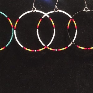 May include: Five pairs of beaded hoop earrings in turquoise, white, black, and red. The earrings are all the same size and shape, but each pair has a different color scheme.
