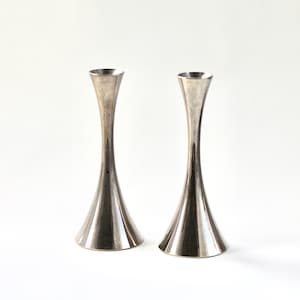 May include: Two silver candle holders with a flared base and a narrow neck.