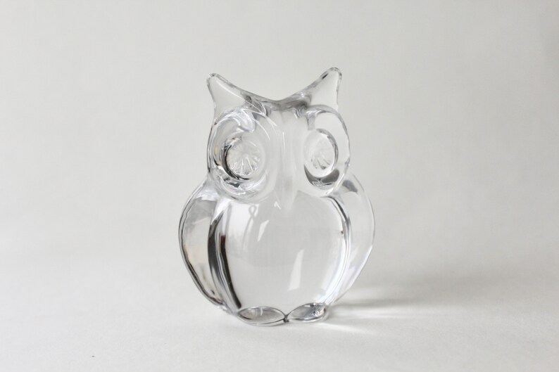 May include: A clear glass owl figurine. The owl has large, round eyes and a detailed beak.