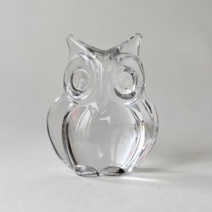 May include: A clear glass owl figurine. The owl has large, round eyes and a detailed beak.