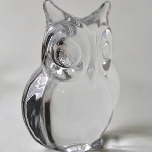 May include: A clear glass owl figurine with detailed eyes. The owl is sitting on a white surface.