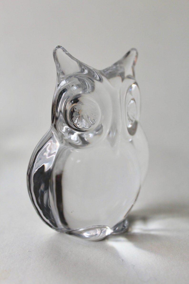 May include: A clear glass owl figurine with detailed eyes. The owl is sitting on a white surface.