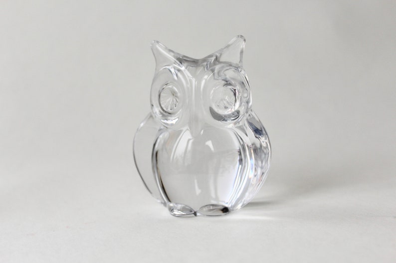 May include: A clear glass owl figurine. The owl has large, round eyes and a detailed, textured body.