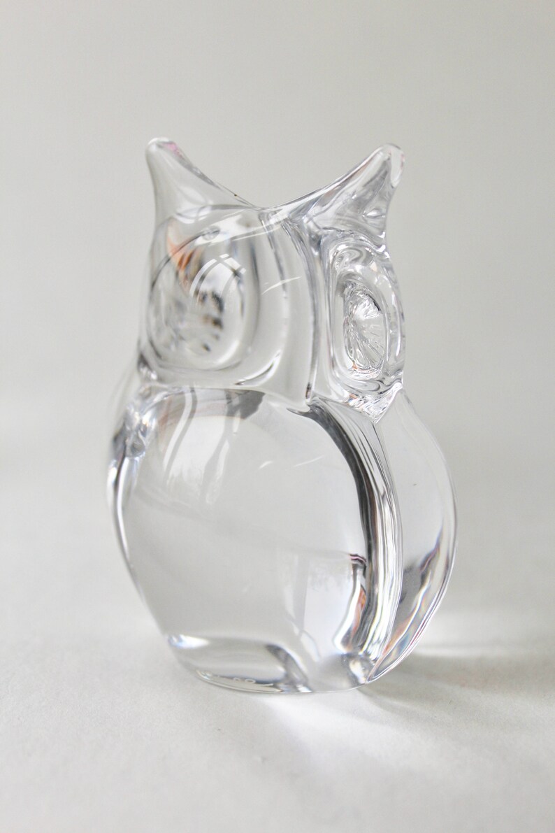 May include: A clear glass owl figurine. The owl is sitting on a white surface.