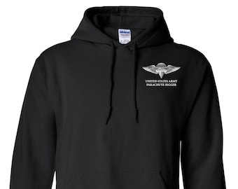 May include: Black hooded sweatshirt with a front pocket and drawstring. The sweatshirt features a white graphic of a parachute and wings, with the text "UNITED STATES ARMY PARACHUTE RIGGER" below the graphic.