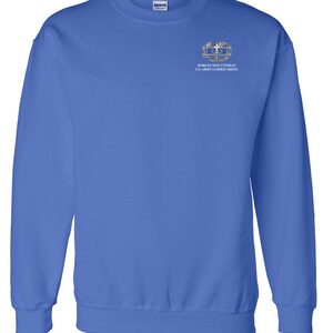 May include: A royal blue sweatshirt with a white embroidered patch on the left chest. The patch features a silver Korean War Veteran U.S. Army Combat Medic insignia.